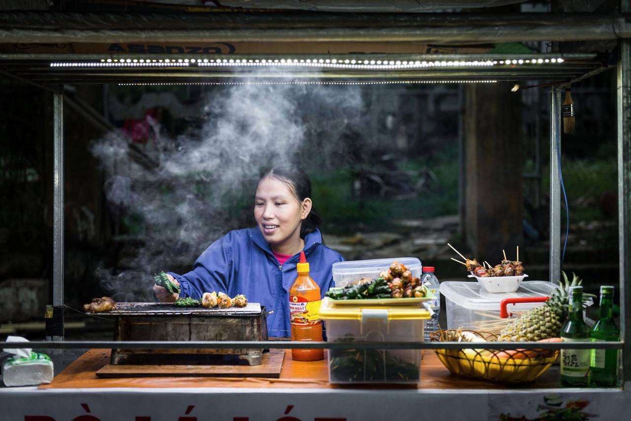 Người phụ nữ nướng xiên thịt tại quầy hàng rong ở Hội An, khói bốc lên từ bếp nướng