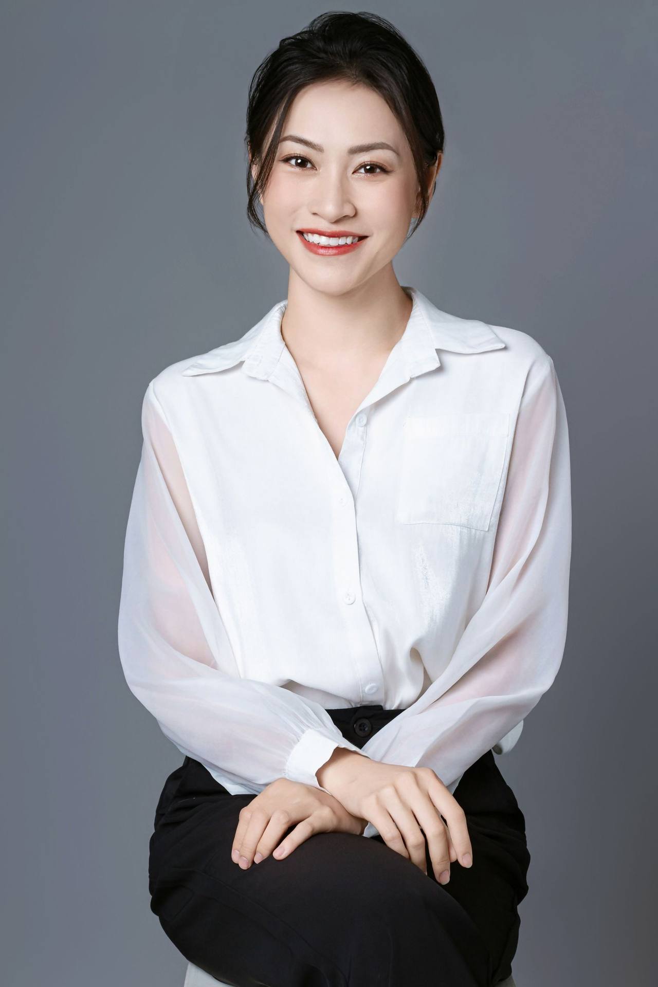 Chân dung người phụ nữ Việt Nam mặc áo sơ mi trắng ngồi mỉm cười trước phông nền xám